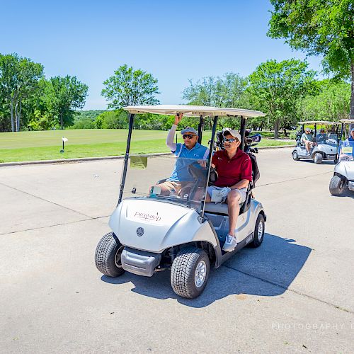 People riding in golf carts on a sunny day, with green trees in the background and a clear blue sky.