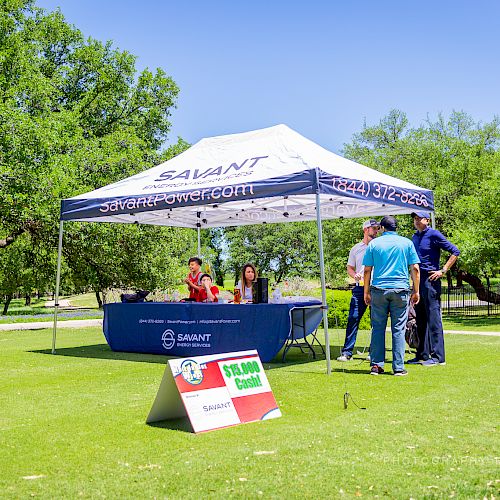 A group of people under a tent on a golf course, with signs for 