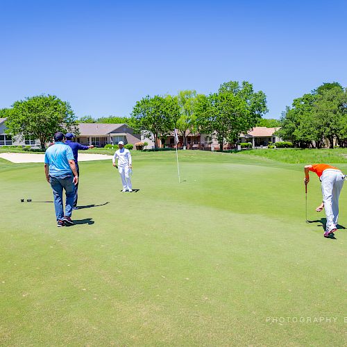 Three people are on a golf course putting green, with one person putting the ball while the others watch.