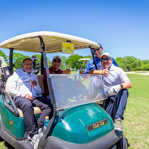 Four people are smiling and posing with a golf cart on a sunny day at a golf course.