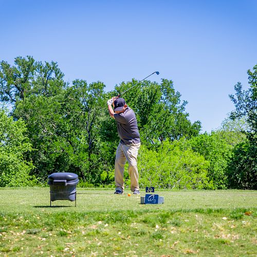 A person is playing golf on a lush green course, surrounded by trees, taking a swing.