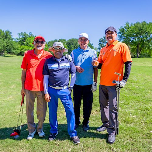 Four men are posing for a photo on a golf course with equipment in hand.