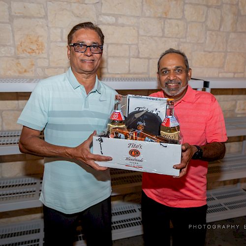 Two men are posing indoors, one holding a decorated gift box. Shelves and a stone wall are in the background. ending the sentence.