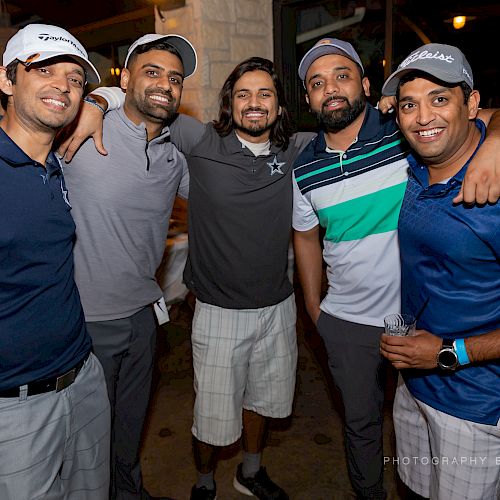 Five men are posing together, smiling, and wearing casual or sportswear. They seem to be having a good time, possibly at a social event.