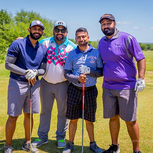 Four men are posing with golf clubs on a sunny golf course, standing closely together and smiling for the camera.