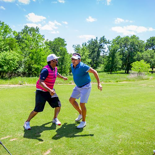 Two individuals are shown on a golf course, engaging in a playful moment, surrounded by lush greenery and trees under a blue sky.