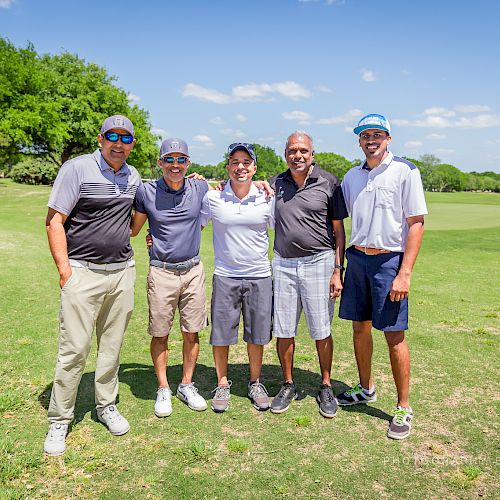 The image shows five people standing together on a golf course, smiling and posing for the photo. They appear to be enjoying a sunny day outdoors.