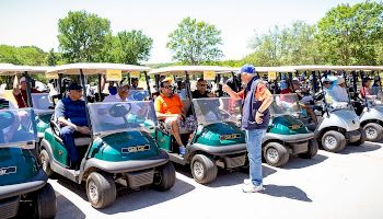 People sitting in golf carts, possibly preparing for a game, while someone gives instructions to the group.