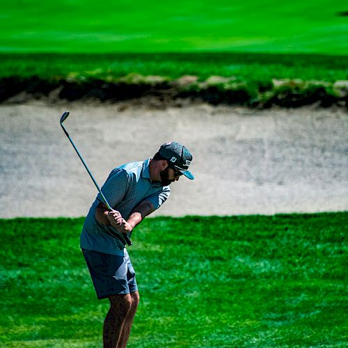 A golfer in mid-swing is on a lush green course with a sand trap in the background, wearing a cap and golf attire.