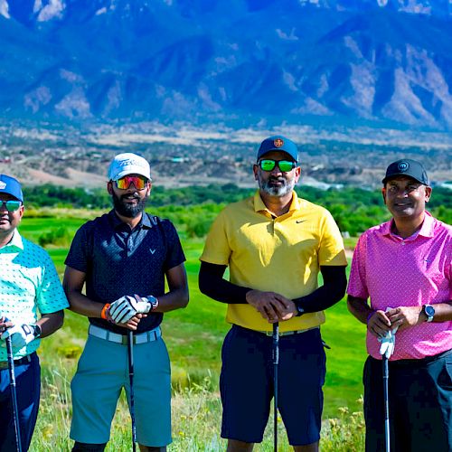 The image shows four individuals posing with golf clubs on a golf course, with mountains in the background.