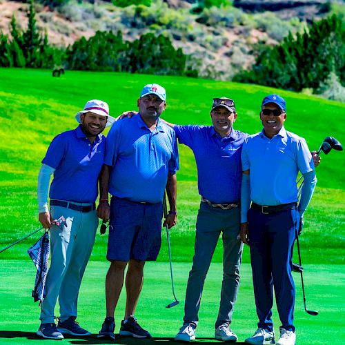 Four men are standing on a golf course, smiling and posing with their golf clubs in hand while wearing golf attire.