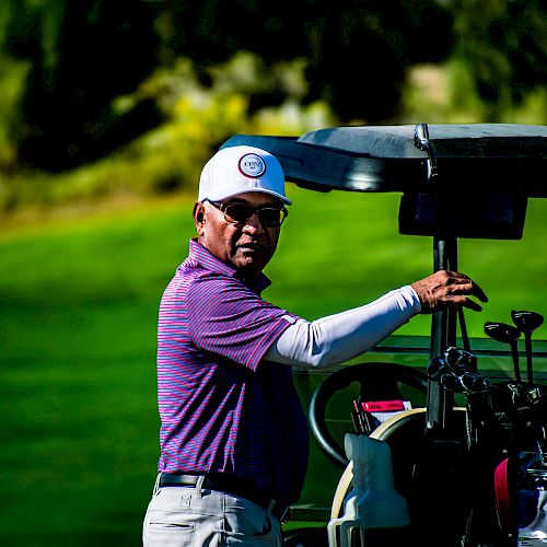 The image shows a person in a purple shirt and white hat standing next to a golf cart on a golf course, with green grass and trees in the background.