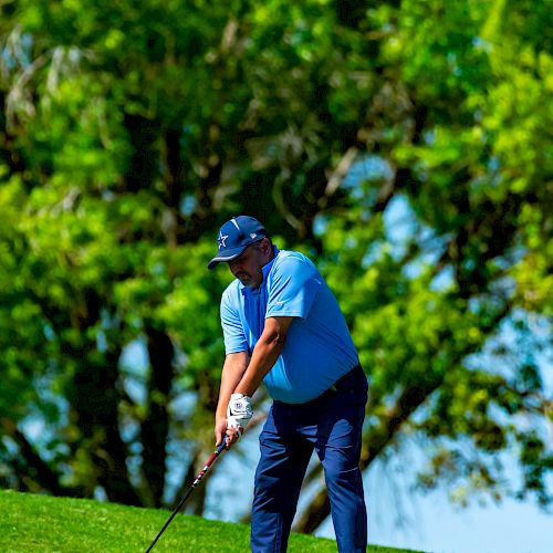 A golfer dressed in blue is preparing to take a shot on a lush, green course with trees in the background.