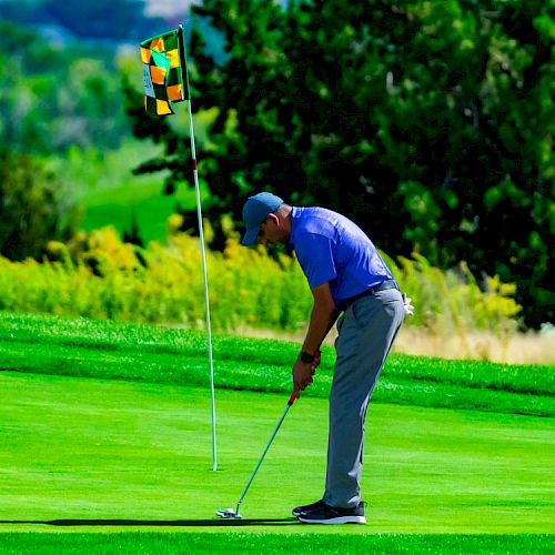 A golfer is putting on a green near a flagstick, surrounded by lush greenery and trees in the background.