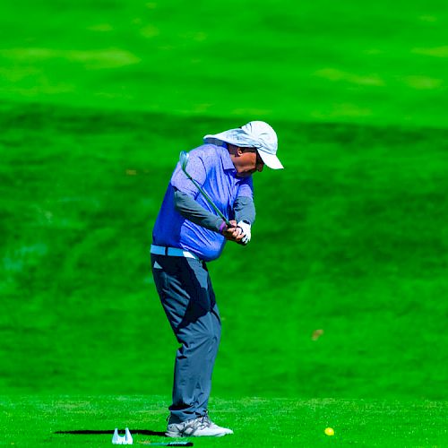 A person dressed in golf attire is swinging a club on a bright green golf course.