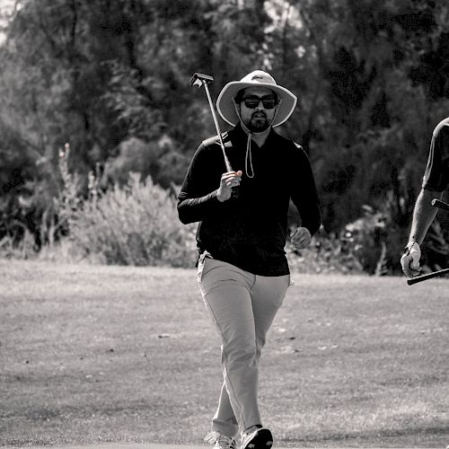 A person wearing a wide-brimmed hat and sunglasses is walking on a golf course holding a golf club. They appear to be enjoying the day outdoors.