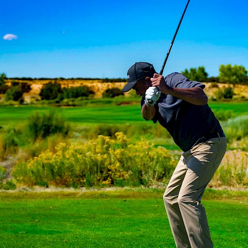 A person is preparing to hit a golf ball with a club on a green golf course with a clear blue sky and landscape in the background.