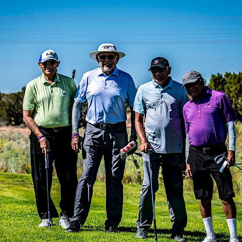 Four men are standing on a golf course holding their clubs on a sunny day.