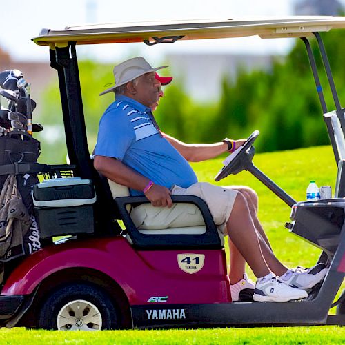 A person in a hat driving a red Yamaha golf cart on a golf course, with golf clubs in the back of the cart, enjoying a sunny day.