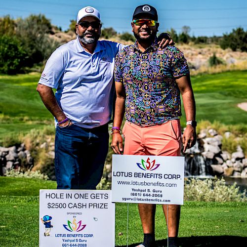 Two men are standing on a golf course beside signs advertising a $2500 cash prize for a hole in one, sponsored by Lotus Benefits Corp.