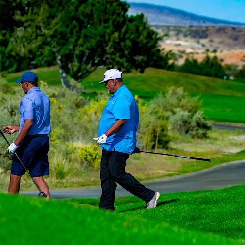 Three people are on a golf course, walking along a path with clubs and gear, surrounded by greenery and distant hills on a sunny day.