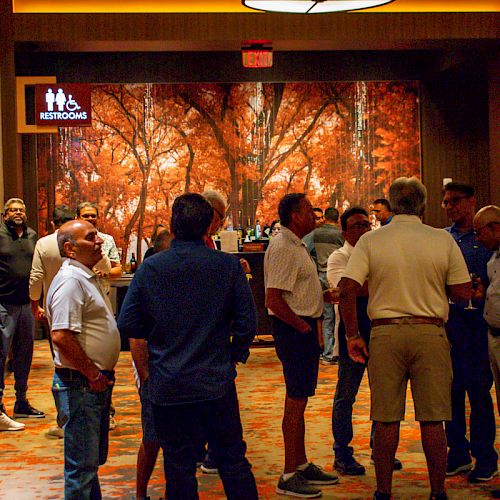 A group of people are gathered in a hallway with autumn-themed decor, near a restroom sign.