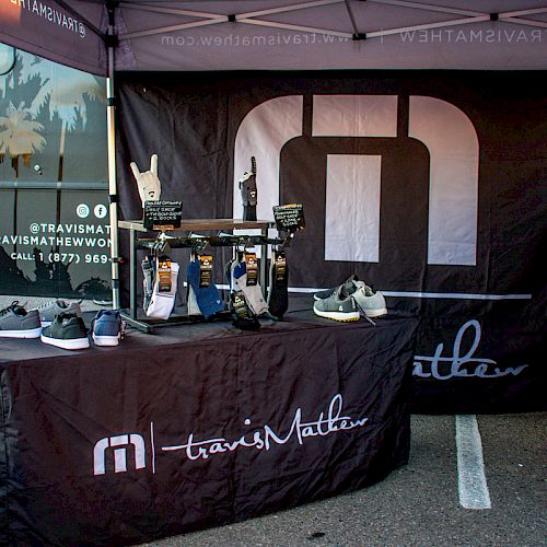 A booth with a banner and table displays branded items, including shoes and accessories. The branding reads 