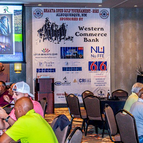 The image shows a group of people seated at tables during an event. A large banner displays sponsors for the Bhava Yog Golf Tournament 2023.