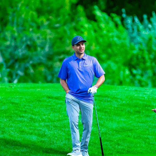 Two people are on a golf course. One is standing and holding a club, while the other appears to be engaging in conversation.