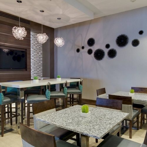 A modern dining area with tables, chairs, decorative wall art, pendant lights, and a TV on the wall.