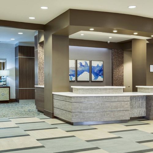 This image shows a modern hotel lobby with a reception desk, decorative lighting, and artwork on the walls.