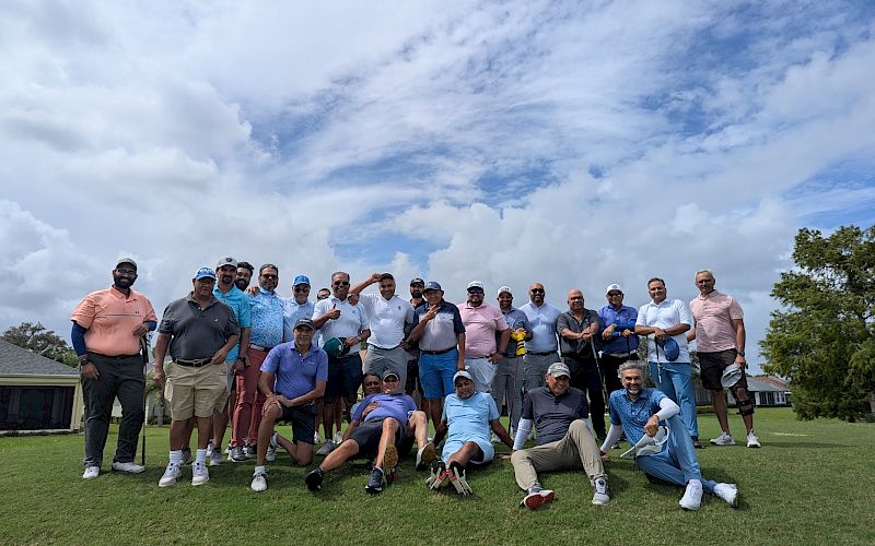 A group of people, casually dressed, are posing on a grassy field under a cloudy sky.