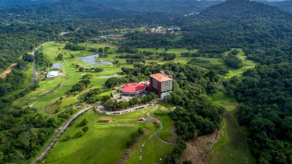 Aerial view of a red-roof resort and buildings amid lush green hills and mountains under cloudy sky.