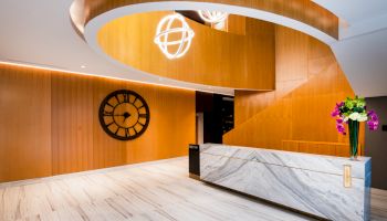The image shows a modern lobby with a marble reception desk, a large decorative clock on the wall, and contemporary light fixtures.