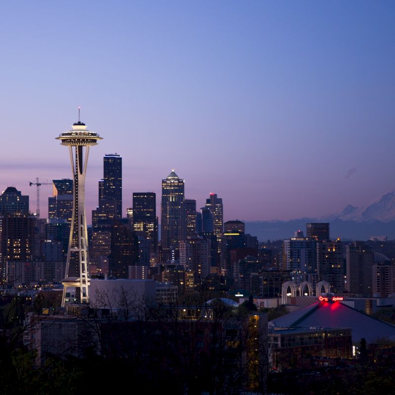 The image shows Seattle's skyline with the Space Needle prominently featured; Mount Rainier is visible in the background during dusk.