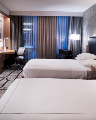 A modern hotel room with two neatly made beds, a wall-mounted TV, a work desk with a chair, and stylish decor, ending the sentence.