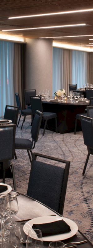 An elegantly set banquet hall with round tables adorned with glassware, silverware, and floral centerpieces. The room is well-lit with overhead lighting.