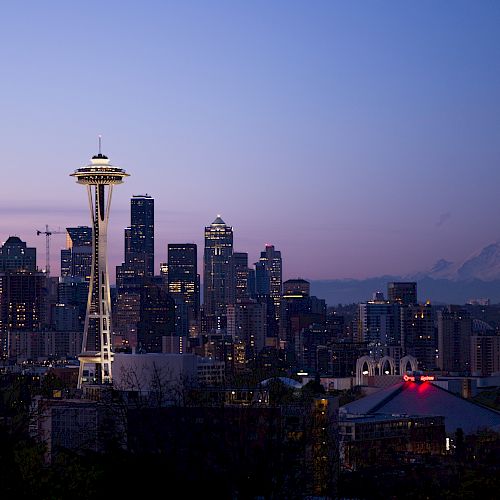 The image shows a cityscape with the iconic Space Needle, skyscrapers, and a mountain in the background at dusk, with the sky transitioning to night.